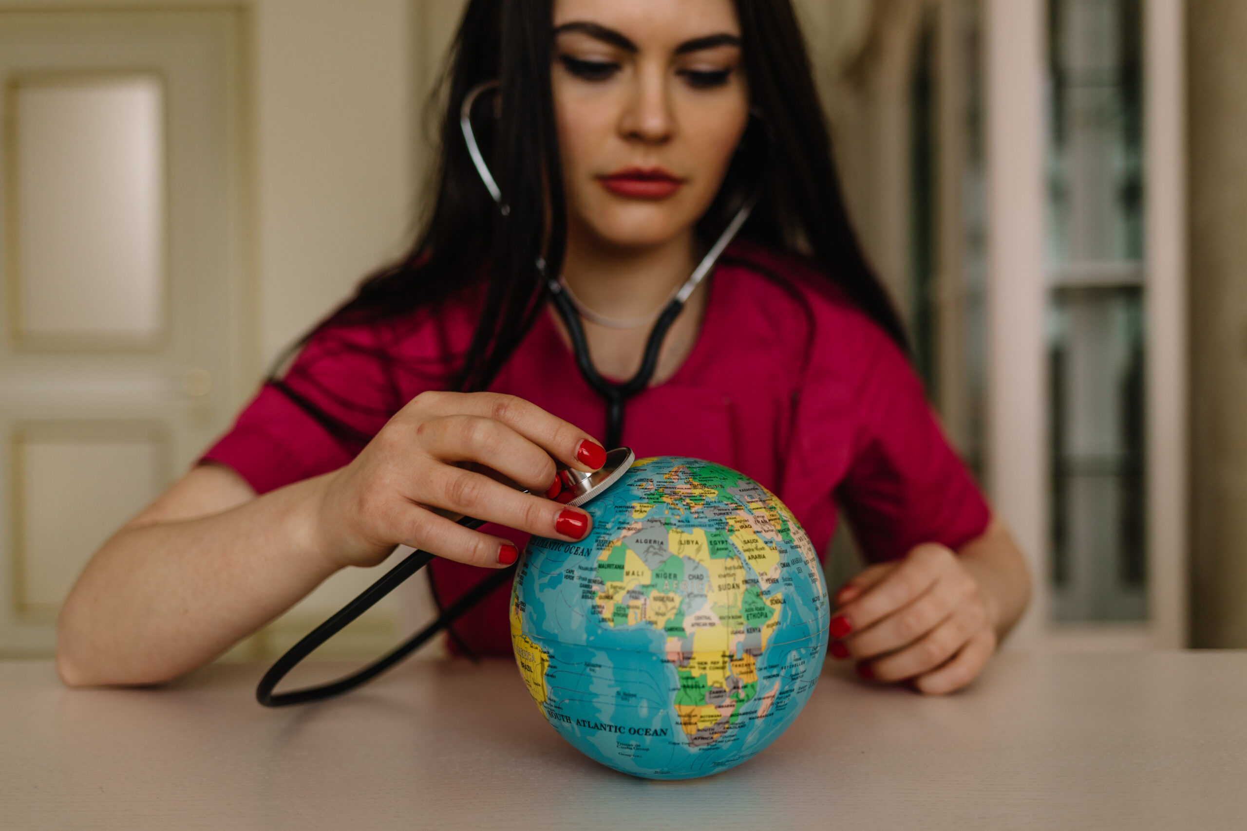 a woman doctor with a stethoscope listening to a miniature globe for World Health Day