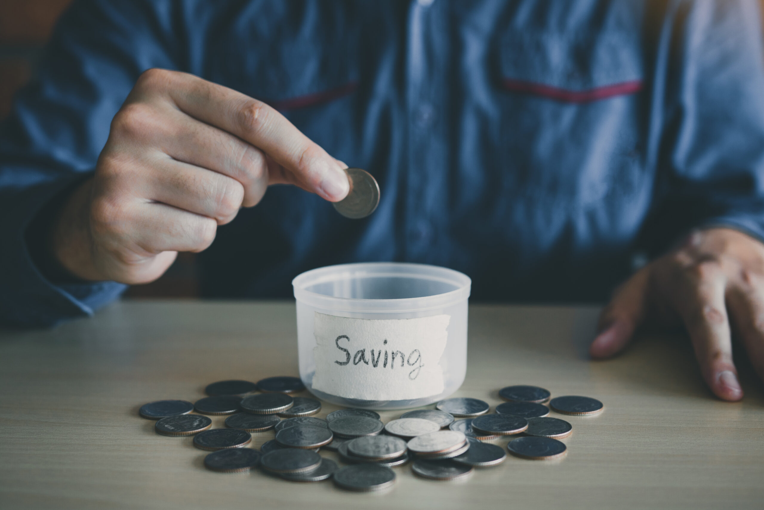 men dropping coins into a container with the word "saving" on it, signifying money management for recovering addicts